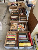Ten cardboard boxes filled with books and magazines on a concrete floor