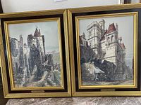 Two framed oil paintings side by side showing architectural scenes of Loire Valley chateaux in layered gold, dark brown and black frames