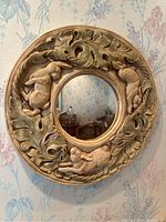 Front view of round animal mirror with dog reliefs and leaf motifs on frame.