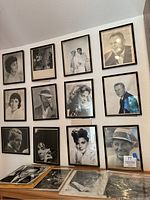 Twelve framed headshots on wall with loose prints on table below