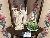 Three Royal Doulton figurines displayed on a wooden shelf with floral wallpaper background.