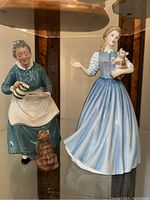 Front view of two Doulton figurines, woman pouring tea with cat, and woman holding cat in blue dress.