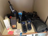 Overview photo showing multiple Braun electric razors, their cords, black zippered cases, and two boxed men's cologne bottles.