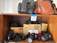 Shelf view showing two camera carry cases on top shelf; Nikon D40x box, D70 outfit box, multiple camera bodies and lenses on lower shelf