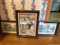 Three framed artworks: central painting and two prints on either side