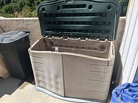 Open Rubbermaid storage bin showing empty interior after contents removed or partial contents visible; hinged lid open.