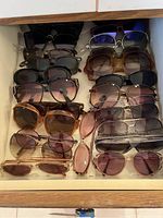 Drawer with multiple pairs of sun glasses in varying colors and styles, mostly tinted lenses