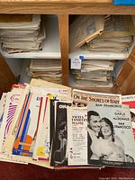 Shelf and cabinet filled with stacks and piles of vintage sheet music with various colorful and monochrome covers.