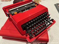 Front three-quarter view of cherry red typewriter with cover partially underneath