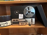 Full view of the Sony TC-350 tape recorder with tape reel on hub, VU meters, control panel, instruction manual, and black box on shelf.