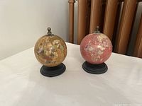 Two mini globes side by side on a white surface, showing front views with black bases and finials on top.
