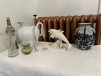 Various assorted decorative glass, ceramic, and porcelain items on a table in front of a radiator including bottles, pitchers, vases, and figurine.