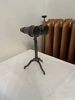 Full view of brass binoculars on tripod against a white background and radiator.