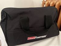 Black Coleman Powermate branded carry bag with handles, displayed on a white surface near a radiator.