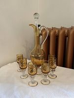 Full decanter and six glasses on a white cloth surface beside a copper-colored radiator