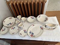 Full view of all dishes laid out on a white tablecloth, showing cups, plates, bowls, serving platter, and gravy boat with floral design.