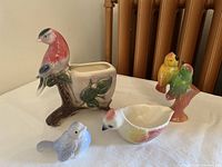 Photo of four ceramic bird-themed knick knacks on white table: planter, bird bowl, small white-blue bird figurine, and colorful pair of birds figurine.