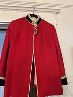 Full front view of the red military jacket hanging on black hanger showing the overall structure, color, and trim details.