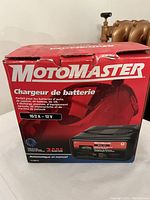 Front of boxed Motomaster battery charger showing brand, charging specs (10/2 A, 12 V), and usage types.