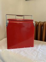 Front view of the red metal cooler showing the carrying handle and smooth finish.