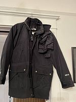 Black The North Face men's jacket hanging on a hanger. Jacket has front zipper and snap closures with two large pockets and Gore-Tex logo on sleeve.