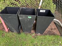 Three black tall plastic planters standing side by side outdoors.