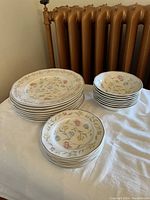 Photo shows stacked vintage china plates and bowls with floral design and silver trim