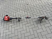 Full view of the gas powered weed wacker showing the shaft, handle, engine and cutting guard.