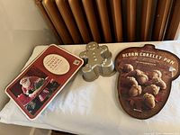 Three baking pans including a rectangular pan with holiday message, gingerbread man mold, and acorn cakelet pan