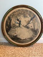 Framed round etching showing full artwork of lady seated with a squirrel in the background with delicate coloring.