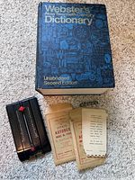 Photo showing the front cover of the 1973 Webster's New Twentieth Century Dictionary along with the black Zephyr Autodex and two refill packs on carpeted floor.