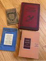 Four vintage and antique books, including a red maroon literary atlas, an anatomy textbook with peach cover, a blue paperback, and a beige paperback with artistic cover.