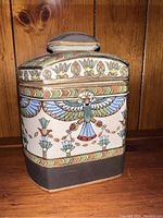 Front and side angled view of the antique Nippon humidor showing detailed hand painted Egyptian style decoration with colorful winged figure and floral motifs, curved ends and lids with knob.