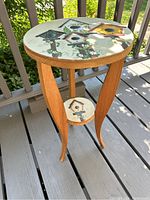 Photo showing round birdhouse table with curved wooden legs and birdhouse painted designs on tabletop and small bottom shelf.