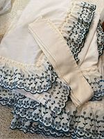 Close-up image showing cream base curtain fabric with detailed forest green eyelet lace trim and folded matching tie backs.