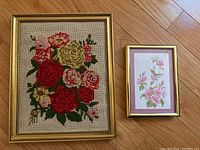 Photo showing both framed needlepoint floral artwork and small floral print side by side on wooden floor.