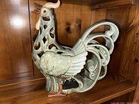 Side view of large ceramic rooster figurine showing cutout body design and rustic blue-green glaze.