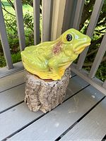 Front angle view of the glossy green and yellow ceramic frog sitting on a hollowed faux log base resembling tree bark.