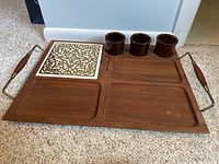 Full top view of cheese board showing four recessed areas, decorative ceramic tile with gold scroll pattern, three small brown ceramic cups.