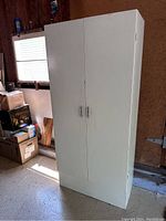 Full view of the closed white metal storage cabinet with two doors, showing handles and overall condition.