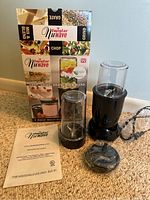 Brand new NuWave Twister multi-purpose chopper blender set, including electric blender base, two clear plastic containers, blades, lid, and instruction manual, box in background.