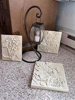 Three stone-like garden wall plaques with raised floral and butterfly patterns arranged on floor and one on an easel.