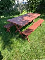 Full view of wooden picnic table and two benches outdoors on grass with sunlight and shadows