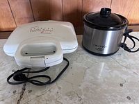 Photo showing the ToastMaster Belgian Wafflebaker closed with handle and power cord on left, and the Crockpot Little Dipper closed with lid on right, both placed on countertop.