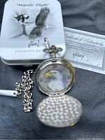 Closed view of the Majestic Flight storage tin, certificate of authenticity, and pocket watch showing the chain and open front cover.