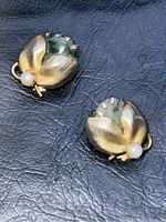 Pair of vintage Kramer clip earrings featuring green jade and white pearls with gold-tone leaf accents on a black textured background.