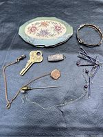 Full view of lot showing Rowenta makeup compact, 14k gold inlaid sterling clasp, chain, key, safety pins and other small jewelry pieces.
