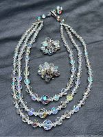 Full view of vintage three-strand crystal necklace and matching clip earrings laid on black background, showing iridescent faceted beads.