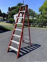 Full view of open orange fiberglass A-frame ladder with aluminum steps and black top cap