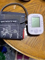 Digital blood pressure meter with connected black adult arm cuff showing brand AolsteCell